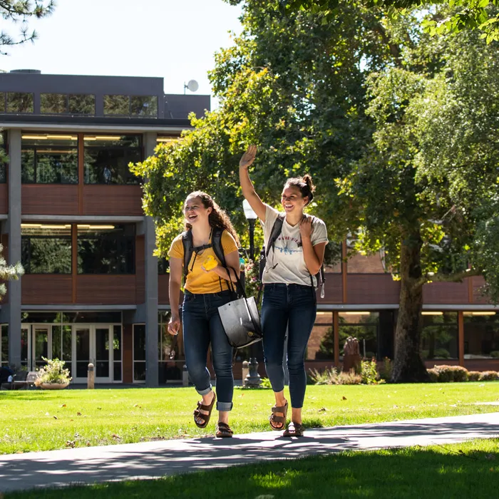 two college students laugh as they walk through a sunny campus at George Fox University